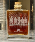 Bottle of 'The Watch 1776-2026' with engraved design on a wooden surface