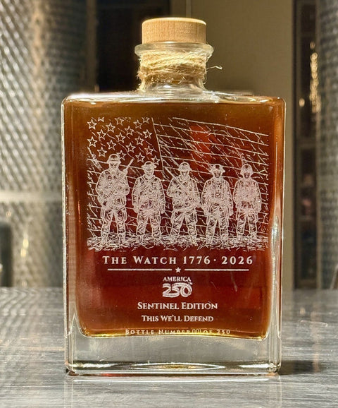 Bottle of 'The Watch 1776-2026' with engraved design on a wooden surface